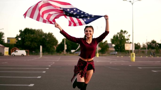 女孩举着美国国旗一边看着镜头一边跑步
