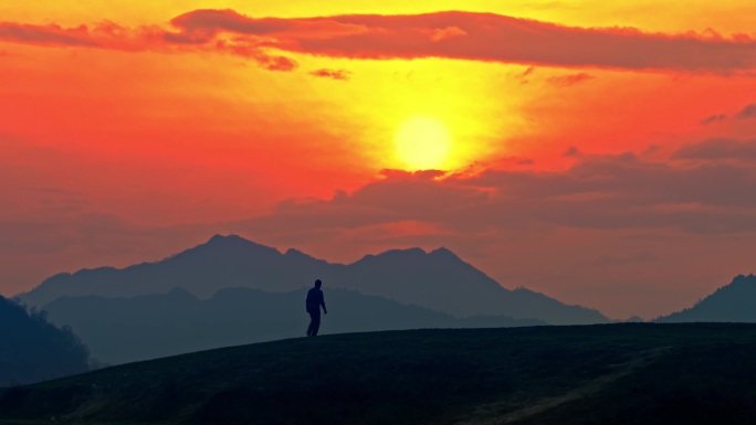 一个人走在群山之间的夕阳下