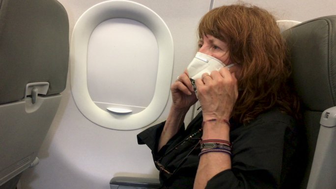 坐在飞机座位上戴着面罩的女士