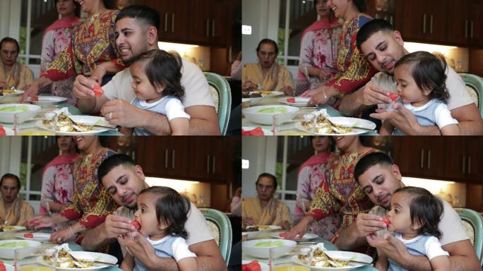 一家人坐着吃午饭时，父亲给儿子喂西瓜。