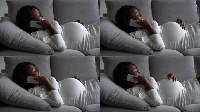 年轻的孕妇躺在家里的沙发上打电话