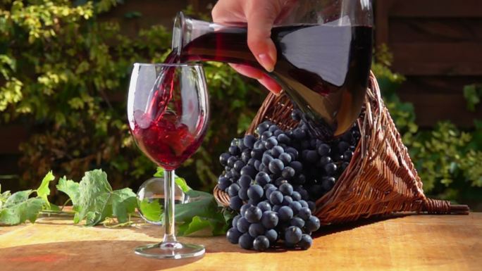 在深紫色葡萄的背景下，红酒从壶中倒入玻璃杯