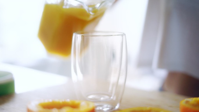 一个女人把橙汁从玻璃罐里倒进玻璃杯里