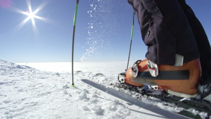 一名滑雪者在山顶上清理雪板上的新雪