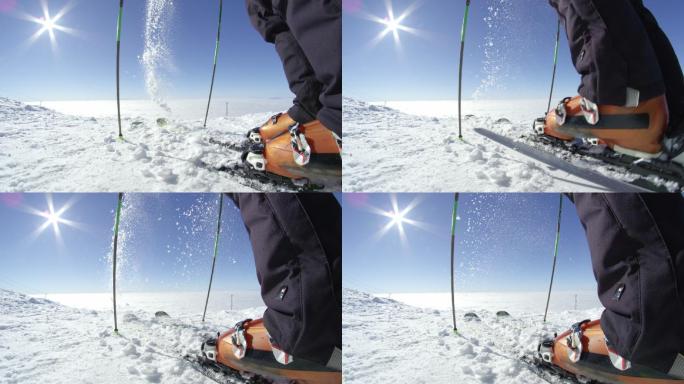 一名滑雪者在山顶上清理雪板上的新雪