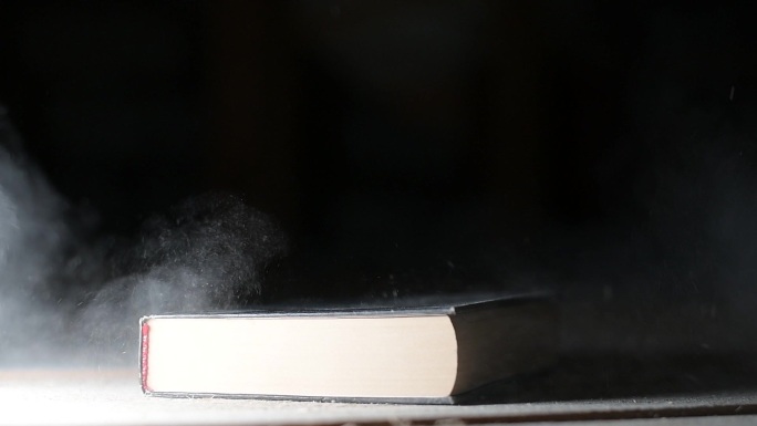 一本书落在满是灰尘的地板上，扬起了灰尘