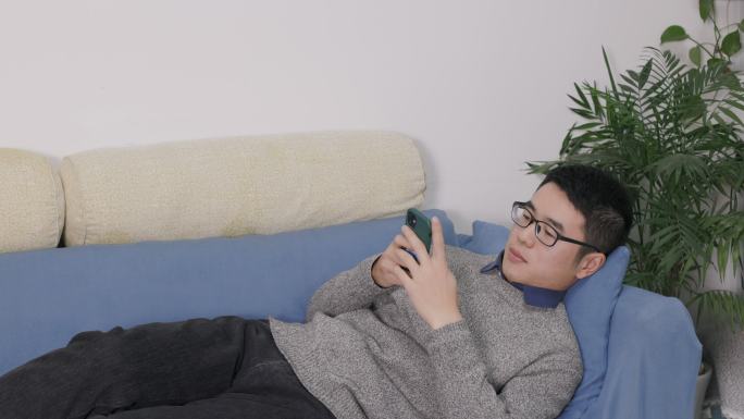4K年轻男性在客厅沙发上躺着玩手机