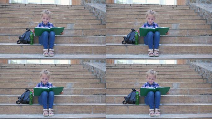 小女孩坐在学校的台阶上背着书包看书