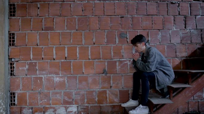 悲伤的少年坐在砖墙旁