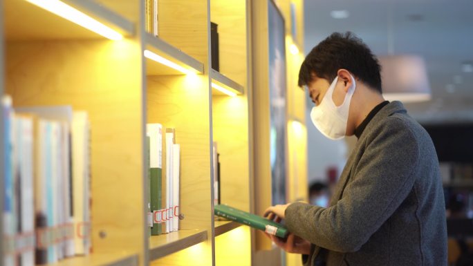 书架前站着翻阅书本的中国年轻男人