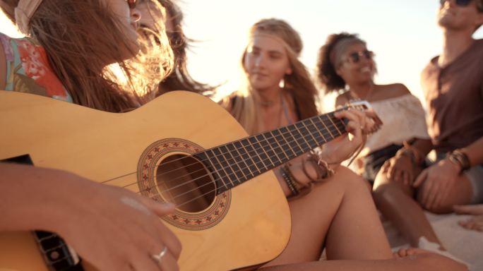和朋友在海滩上弹吉他的女孩