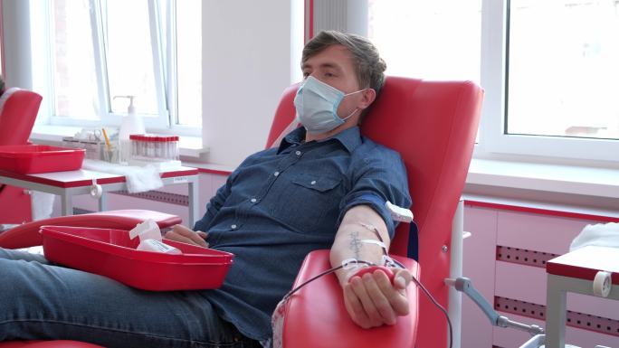 坐在椅子上戴着医用面罩的男子在献血