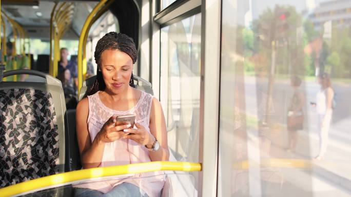 乘公共汽车和使用智能手机旅行的年轻女子