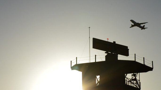 日落时分在机场雷达电信塔上空起飞的飞机