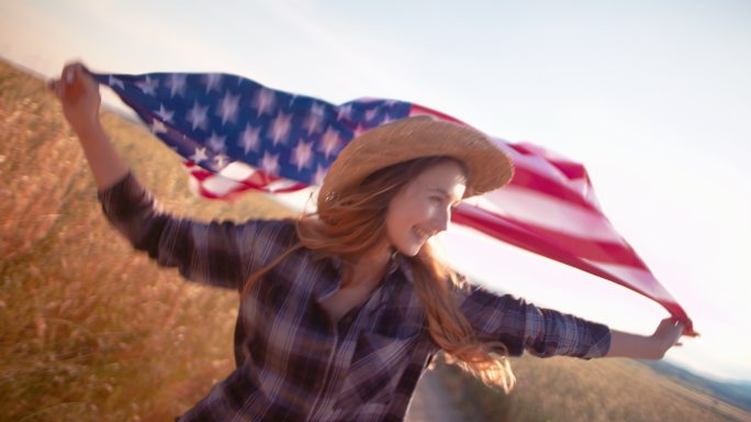 年轻女子手持美国国旗在金色的田野中奔跑