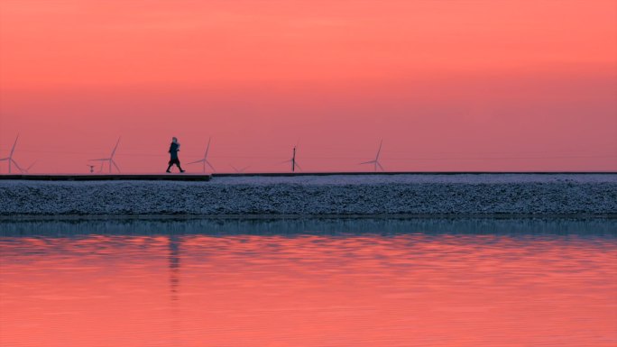 冬天夕阳雪山湖面下孤独行走的一个少女剪影