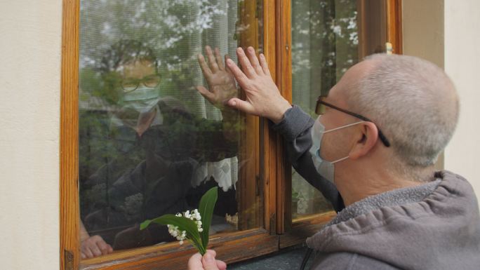 戴面具的老年人通过窗户玻璃进行交流。
