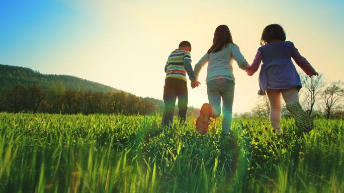 三个孩子手牵着手在阳光明媚的草地上奔跑