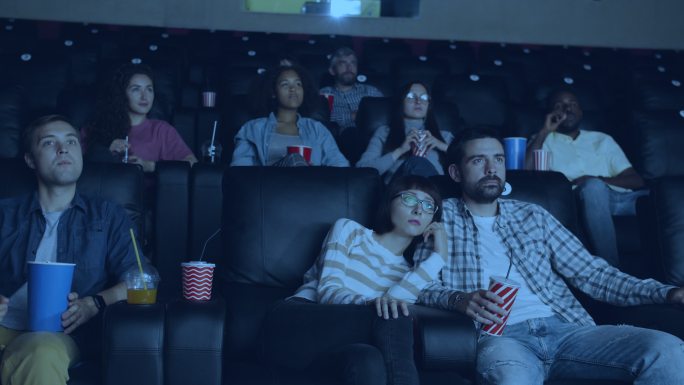 成年人拿着饮料和零食在现代电影院看电影