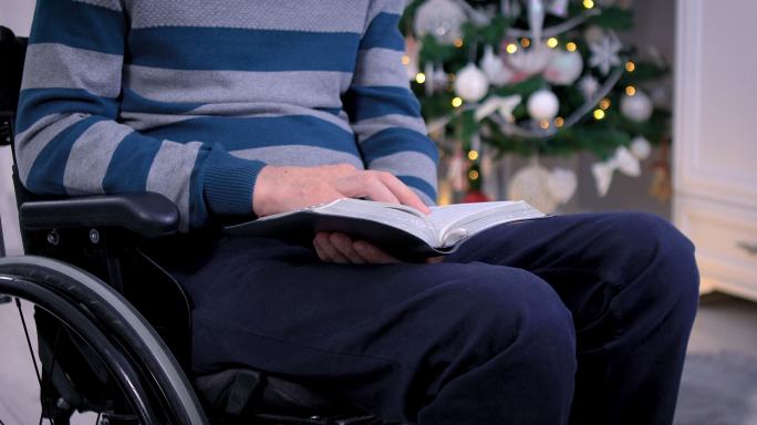 坐轮椅的人在圣诞树前读圣经
