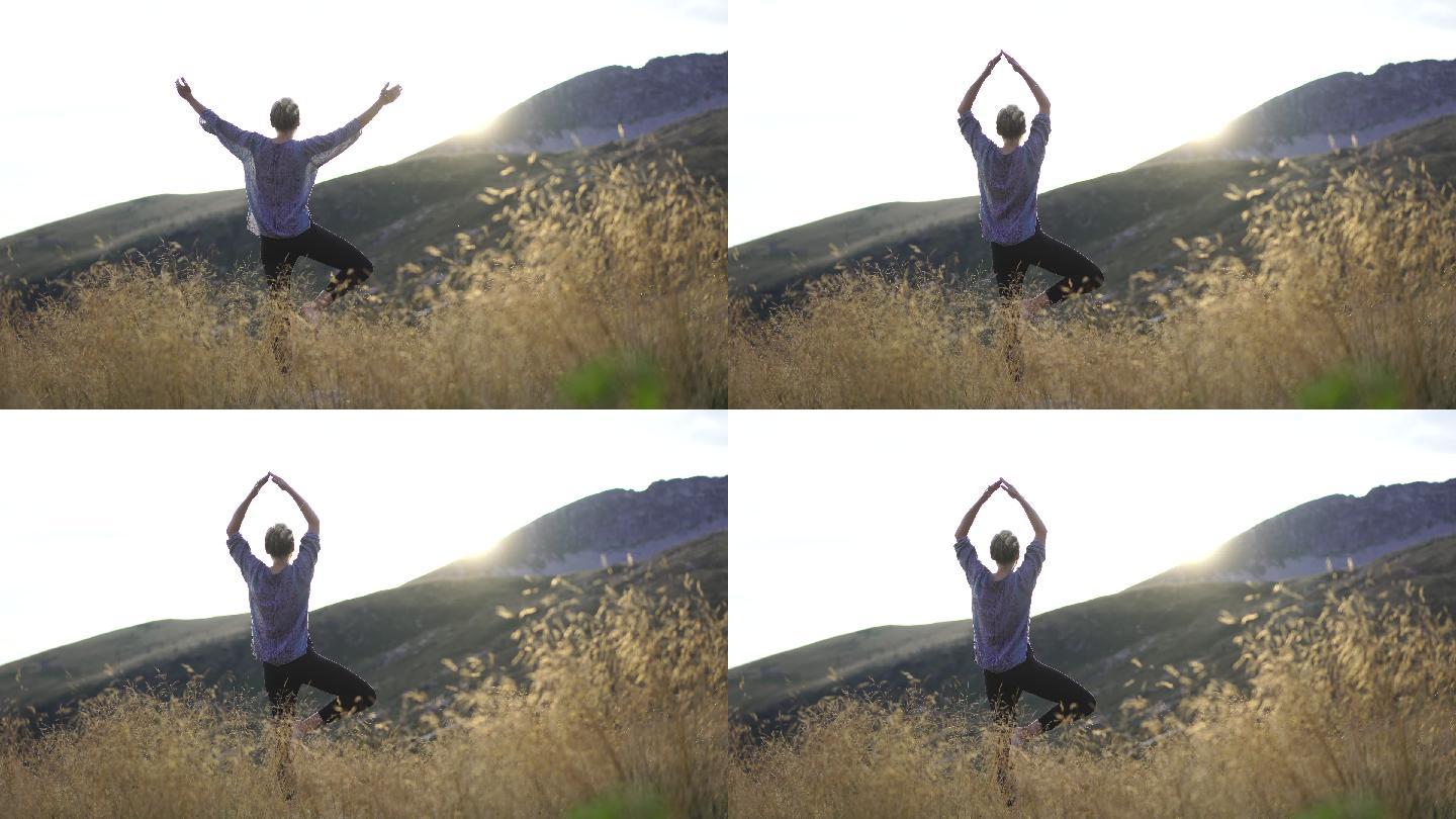 日落时，年轻女子在山顶的高草中做瑜伽