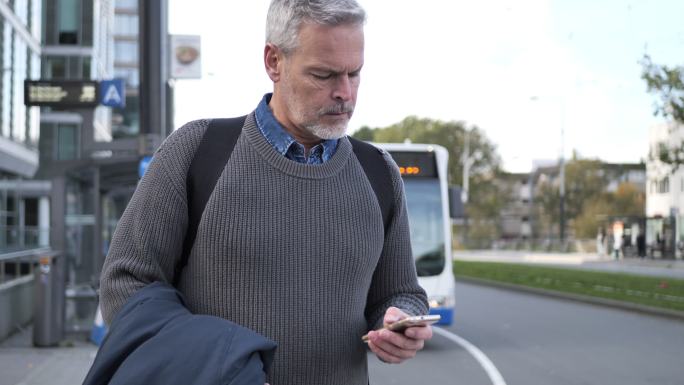 白发男人在秋季通勤时使用智能手机