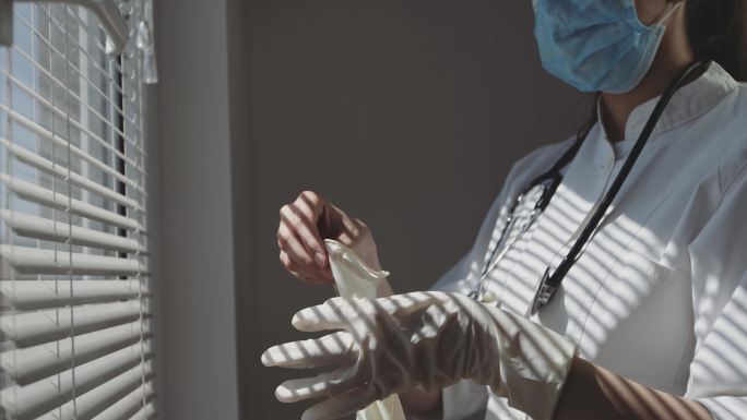 医务护士在窗边戴上医用手套。