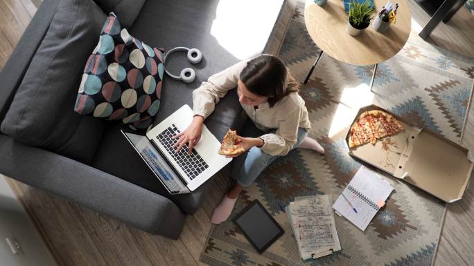 在家里吃比萨饼和使用笔记本电脑的女人