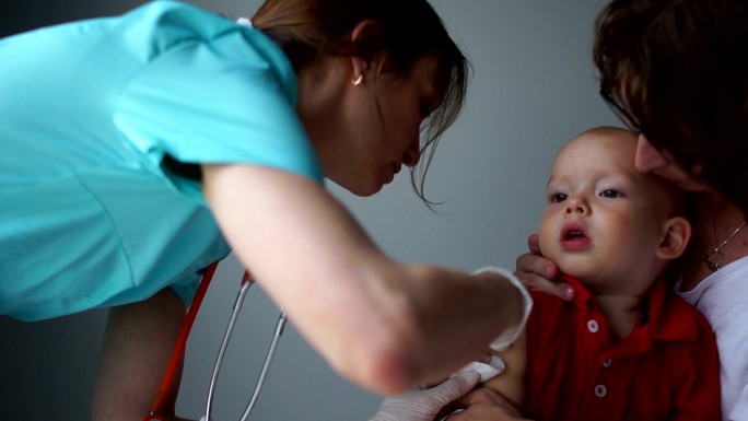 医生给坐在母亲怀里的婴儿接种疫苗