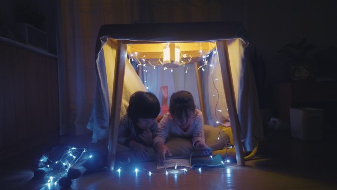 男孩和女孩晚上在自制的帐篷里看书