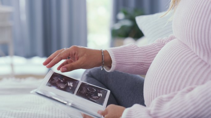 一位母亲坐在床上看着婴儿的的超声波图像