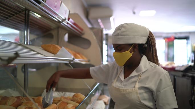 一位女性面包师戴着口罩拿起面包的画像