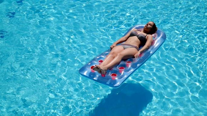女孩躺在游泳池的木筏上晒日光浴