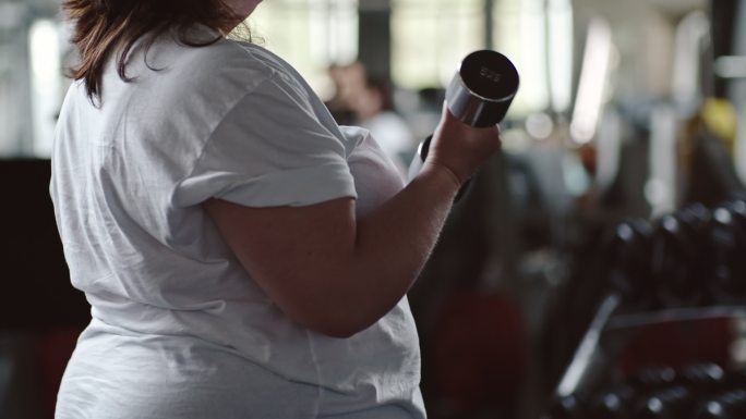 超重妇女站在健身房做前两个哑铃举操