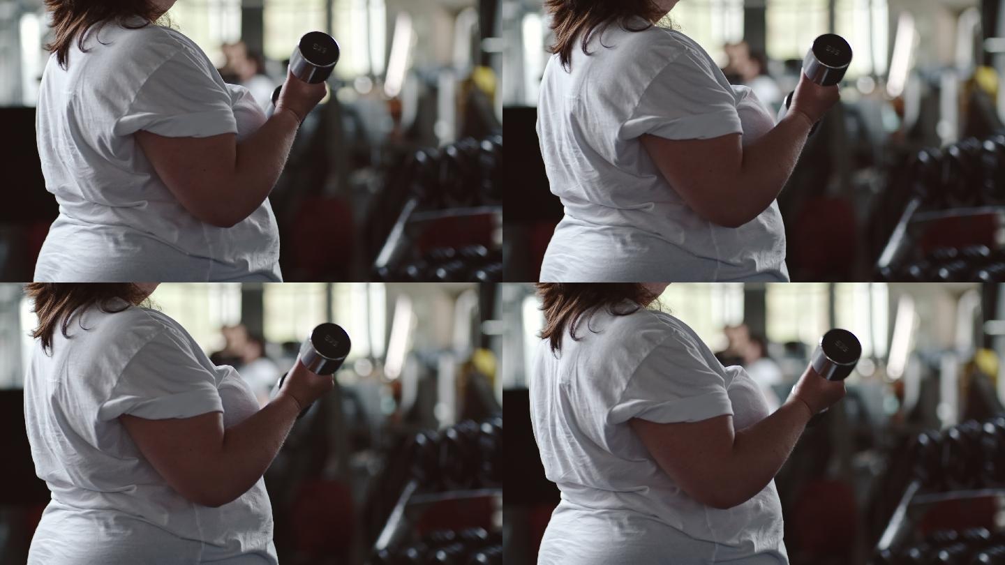 超重妇女站在健身房做前两个哑铃举操
