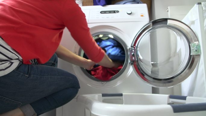 女人从洗衣篮里拿出衣服，放进洗衣机