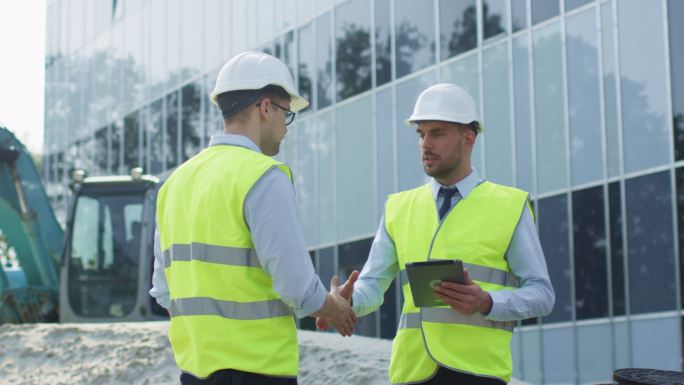 两名戴安全帽的工程师在建筑工地握手同意