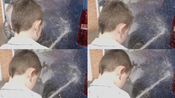 一个小男孩正在用肥皂海绵和软管冲洗车