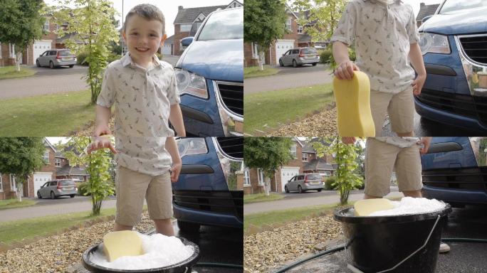 小男孩正在用肥皂海绵和软管冲洗他父母的车