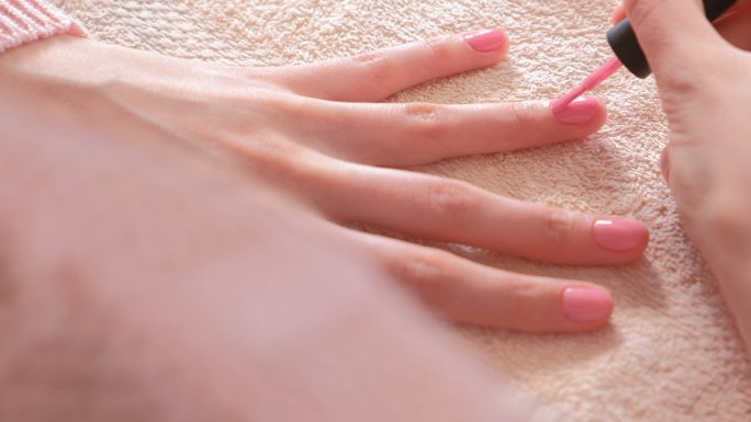 一位女士在指甲上涂了第二层粉色甲胶。