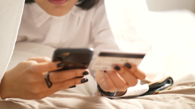 一名妇女用信用卡在卧室里网上购物