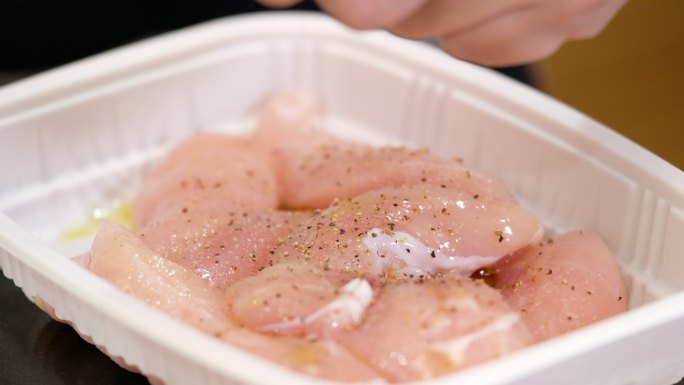 用手把生鸡肉放在厨房台面的塑料托盘里腌制