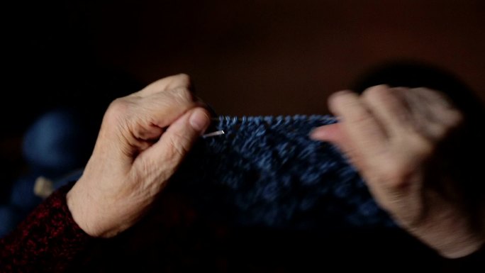 老妇人坐在家里织衣服。