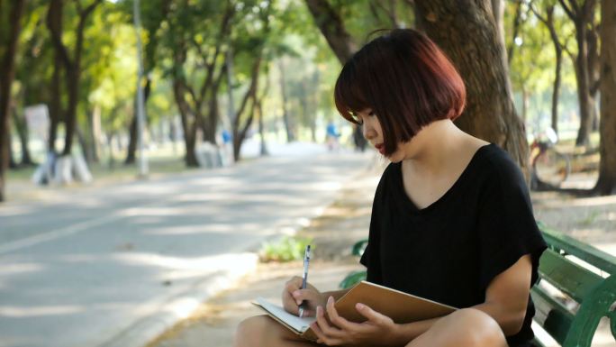 在公园里写日记的快乐时髦女人。