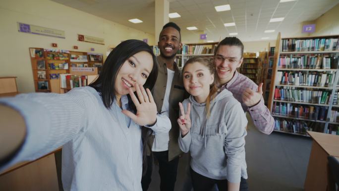 国际学生团体在大学图书馆室内用智能手机自拍和微笑