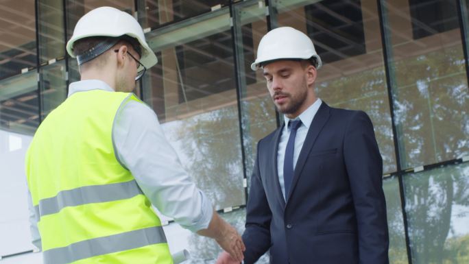 戴安全帽的商人和工程师在建筑工地握手