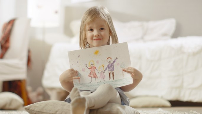 可爱的小女孩坐在枕头上展示她的绘画