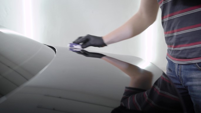 在车间里，一名男子擦拭着一辆汽车的车盖。