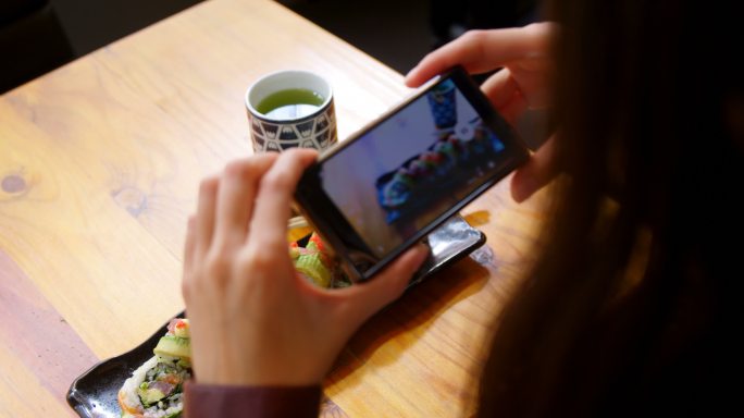 在餐厅用手机拍寿司的女人
