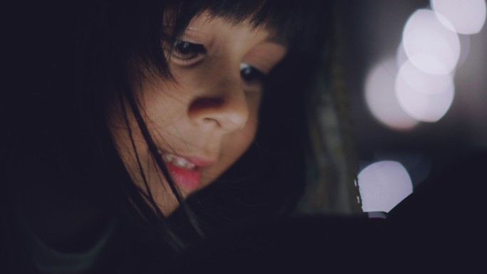 一个女孩在黑暗中玩智能手机游戏。
